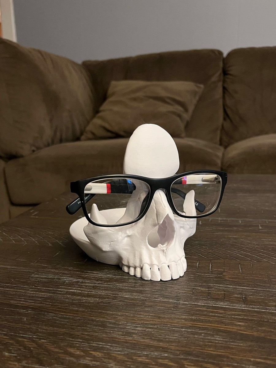 White skull-shaped holder supporting a pair of glasses on a table