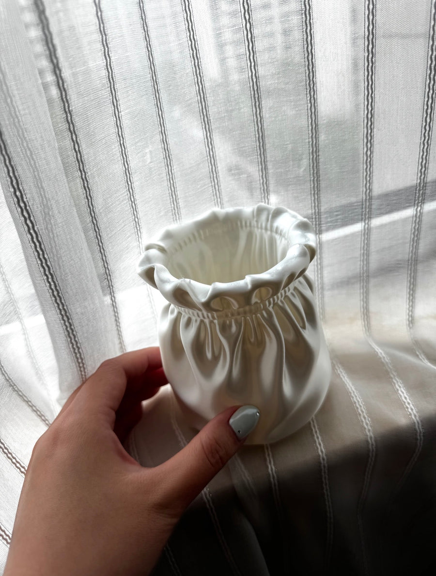 White vase with sculpted folds held beside a window